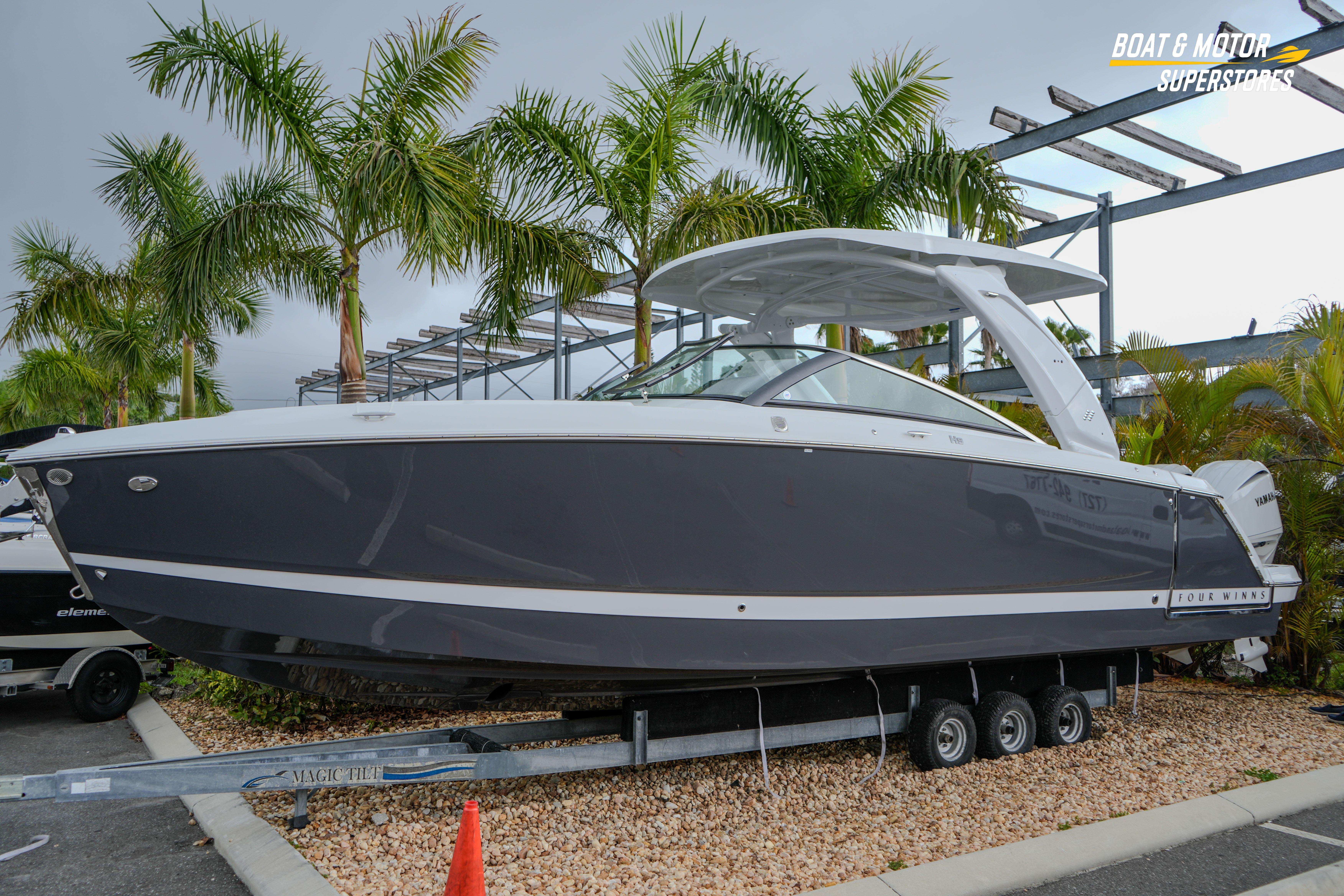2026 Four Winns H9 OB boat on trailer, surrounded by palm trees.