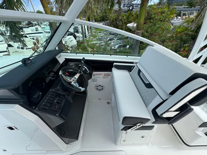  Yacht Photos Pics 2026 Blackfin 302 DC boat cockpit with modern steering and seating, surrounded by lush greenery.