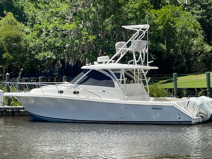  Yacht Photos Pics 2021 Pursuit OS 385 Offshore boat docked by lush greenery.