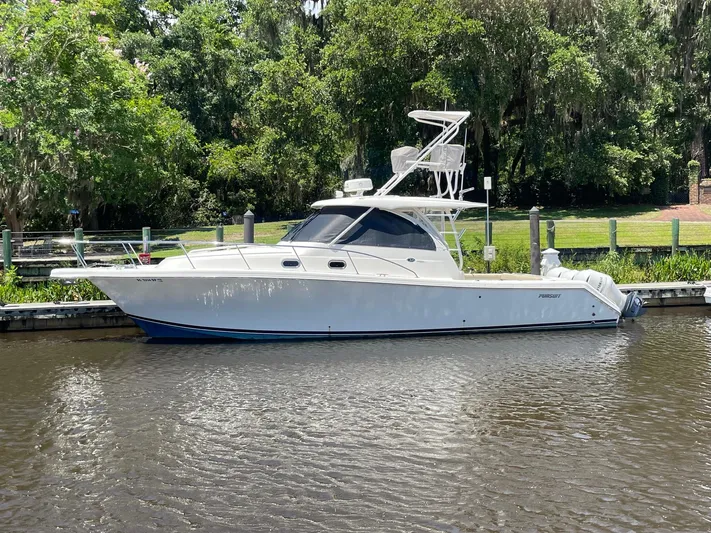  Yacht Photos Pics 2021 Pursuit OS 385 Offshore boat docked on a calm river with lush greenery.