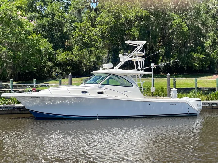  Yacht Photos Pics 2021 Pursuit OS 385 Offshore boat docked by lush greenery.
