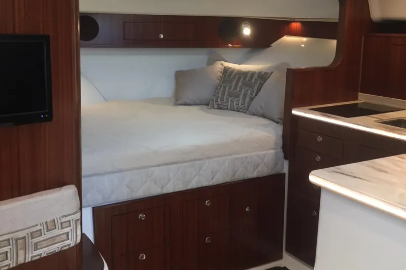  Yacht Photos Pics 2021 Pursuit OS 385 Offshore cabin interior with bed, wood cabinetry, and kitchenette.