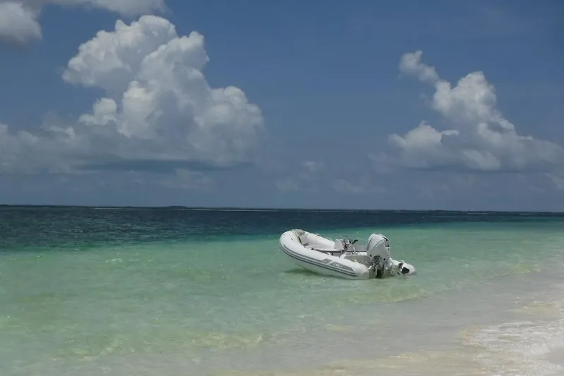  Yacht Photos Pics Inflatable boat on turquoise water near sandy beach under cloudy sky.