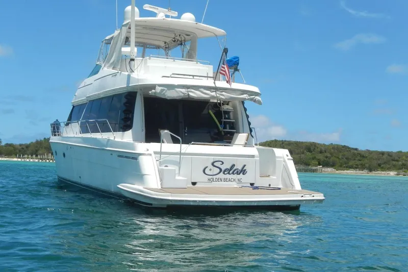  Yacht Photos Pics 2001 Carver 570 Voyager Pilothouse yacht on serene blue waters near a lush shoreline.
