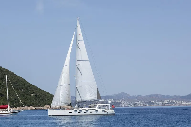  Yacht Photos Pics 2020 Jeanneau 64 sailing yacht on calm sea with distant coastline and hills.