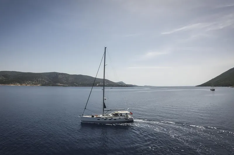  Yacht Photos Pics Sailing yacht Jeanneau 64 (2020) cruising on calm sea with scenic mountain backdrop.