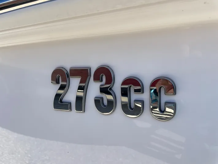 #339 White Yacht Photos Pics Close-up of 2023 Everglades 273CC model emblem on white surface.