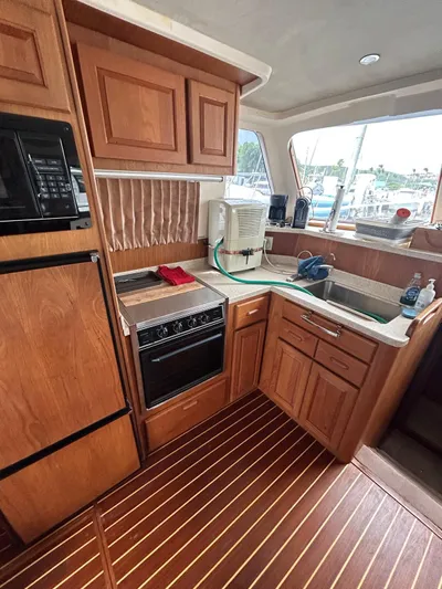  Yacht Photos Pics 1999 Mainship 350 Trawler kitchen with wooden cabinetry, appliances, and a window view.