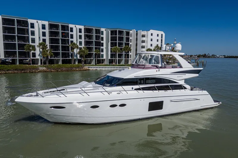 No Vacansea Yacht Photos Pics 2016 Princess Flybridge 64 Motor Yacht on calm water near modern buildings.