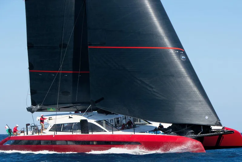 Highland Fling 18 Yacht Photos Pics 2023 Gunboat 80 sailing yacht with black sails and red hull on open water.