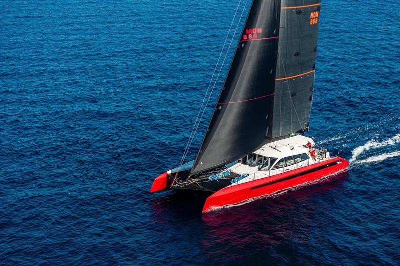 Highland Fling 18 Yacht Photos Pics 2023 Gunboat 80 sailing catamaran with red hull and black sails on open blue sea.