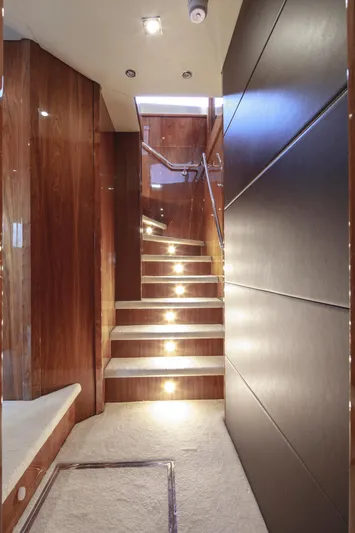 Merci Yacht Photos Pics Luxurious interior staircase of 2010 Sunseeker 88 Yacht, featuring elegant wood paneling and ambient lighting.