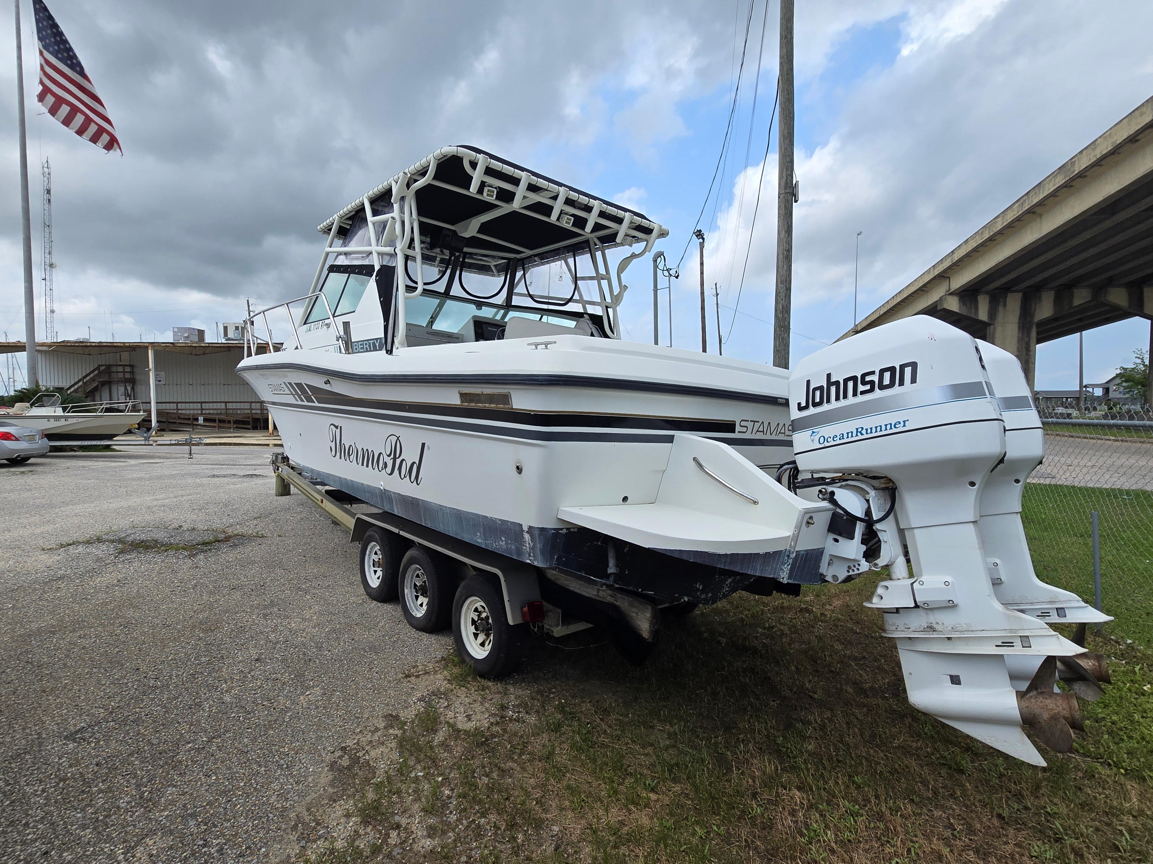 1992 Stamas 288 Liberty boat with Johnson outboard motor on a trailer, parked near a bridge.