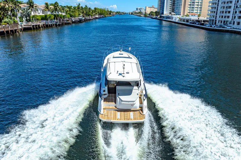  Yacht Photos Pics 2024 Beneteau Gran Turismo 45 cruising on a scenic waterway, surrounded by buildings and palm trees.