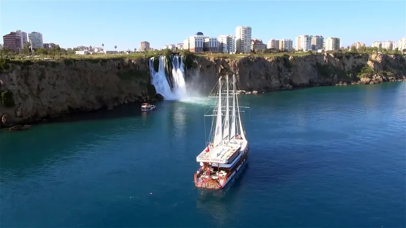 My Dream Yacht Photos Pics Sailing ship Manavgat GT 457 near a coastal waterfall with cityscape in the background.