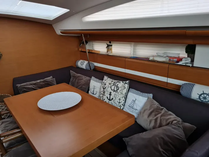  Yacht Photos Pics Cozy interior of 2015 Jeanneau 57 yacht with nautical-themed cushions and wooden dining table.