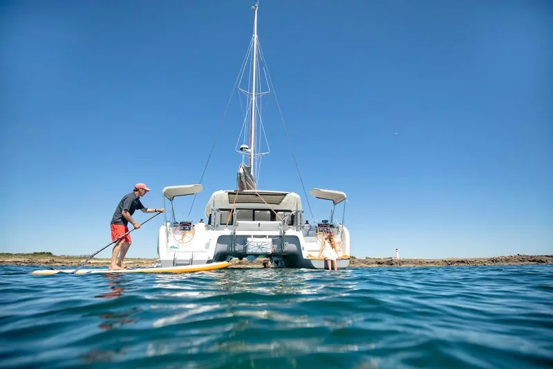  Yacht Photos Pics Man paddleboarding near 2026 Excess 11 catamaran on a sunny day.