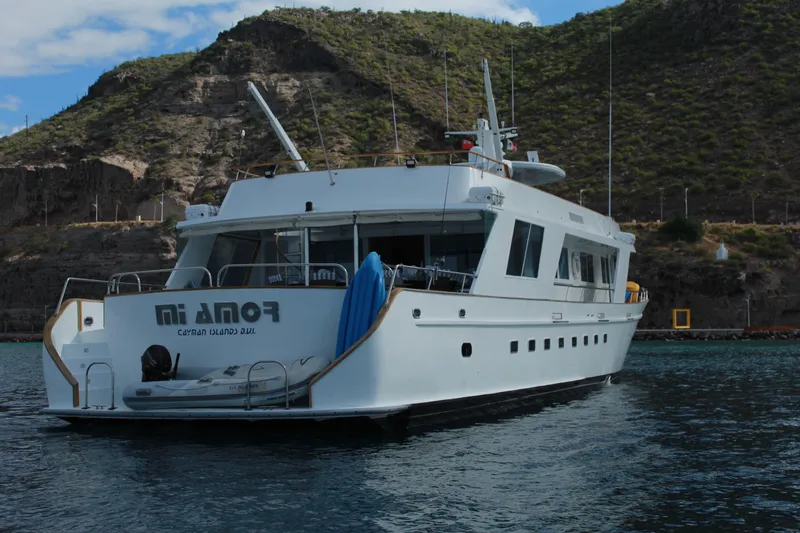 Mi Amor Yacht Photos Pics 1984 DeFever 120 yacht anchored near rocky coastline under a partly cloudy sky.