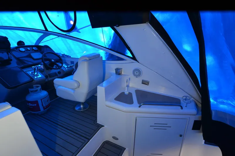 Seeking Sara Yacht Photos Pics 2003 Cruisers Yachts 4370 Express cockpit with steering wheel, seating, and kitchenette under blue cover.