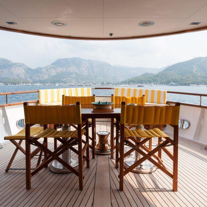 Outdoor dining area on 1984 Codecasa 26m yacht with scenic mountain view.