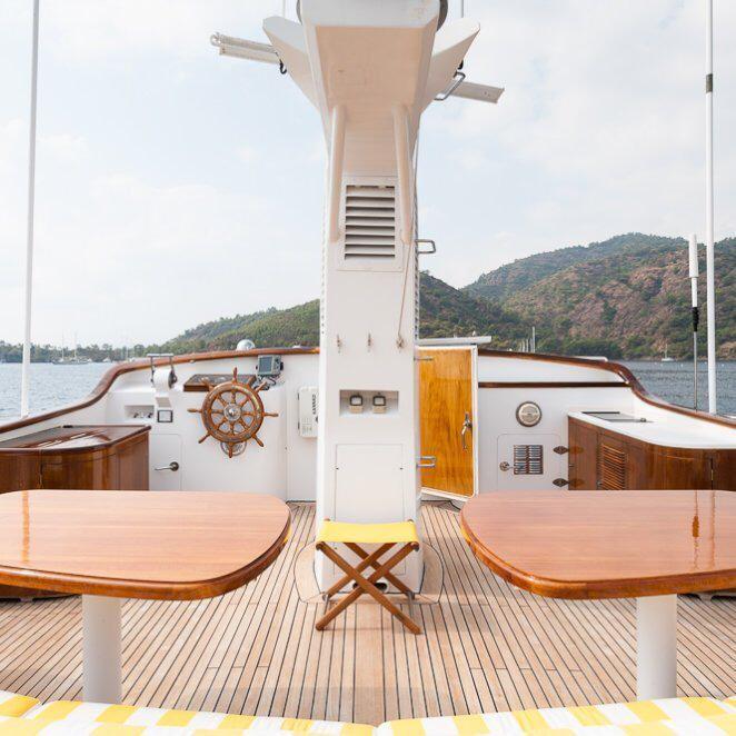 Vintage 1984 Codecasa 26m yacht deck with wooden tables, scenic mountain backdrop.