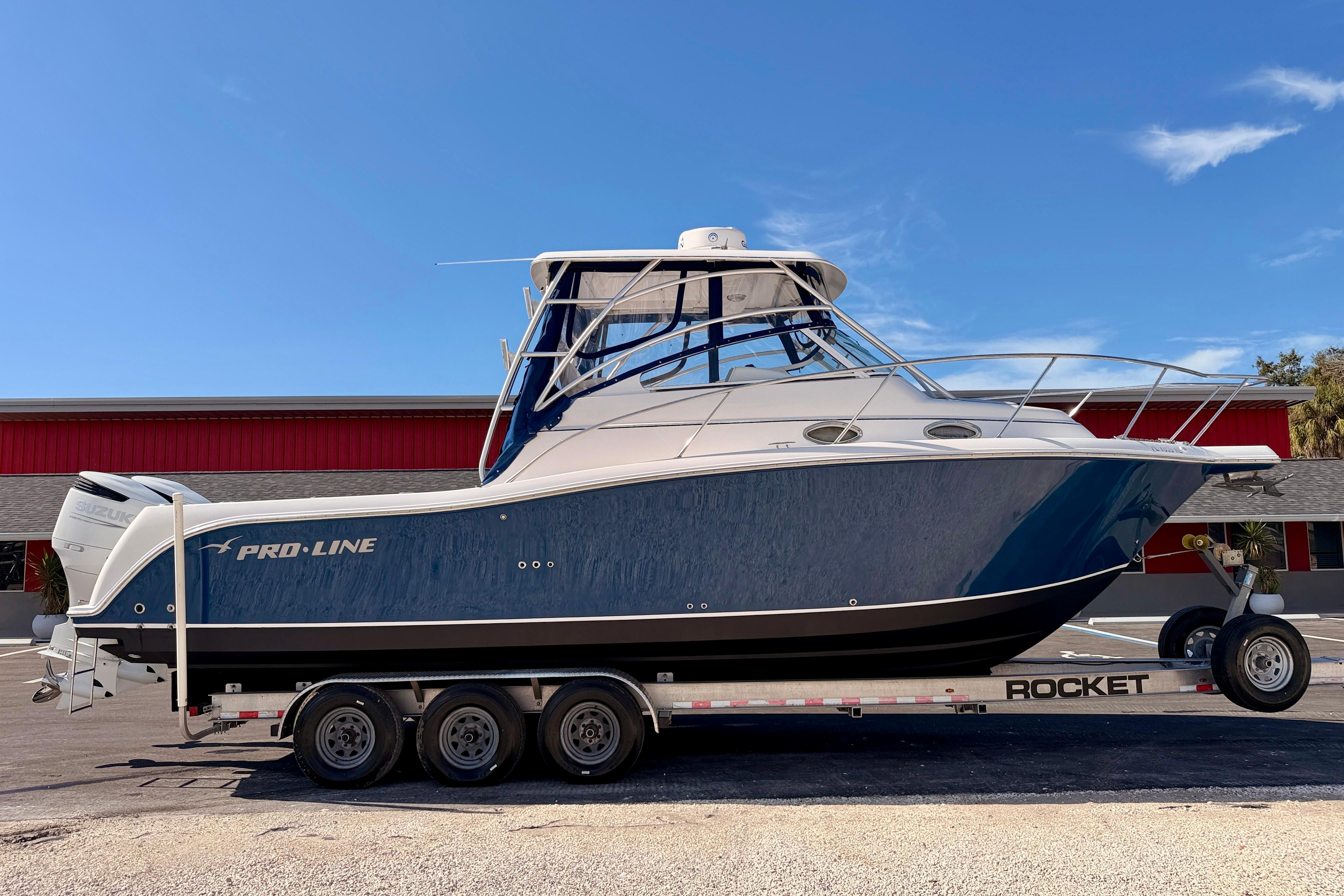 2007 Pro-Line 32 Express boat on trailer, blue hull, parked outdoors.
