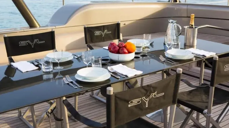 Syl Yacht Photos Pics Luxurious yacht dining setup with fruit bowl, champagne, and SYL-branded chairs on deck.