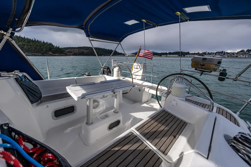 Salus Yacht Photos Pics 2001 Jeanneau Sun Odyssey 40 sailboat cockpit with seating, table, and steering wheel on calm waters.