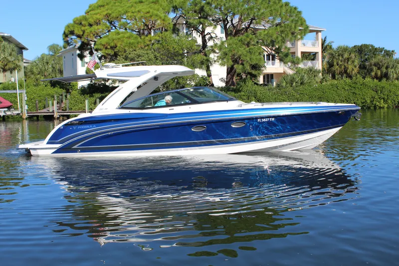  Yacht Photos Pics 2023 Formula 330 Crossover Bowrider on calm water, surrounded by lush greenery.