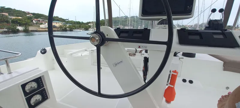 Amea Yacht Photos Pics Steering wheel of a 2014 Lagoon 52 F yacht, docked in a scenic marina.