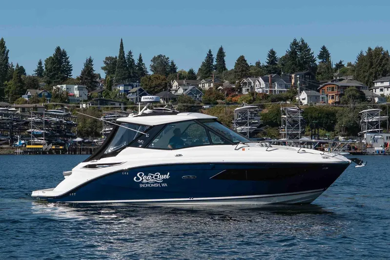  Yacht Photos Pics 2023 Sea Ray Sundancer 320 Coupe cruising on a scenic waterfront with houses in the background.