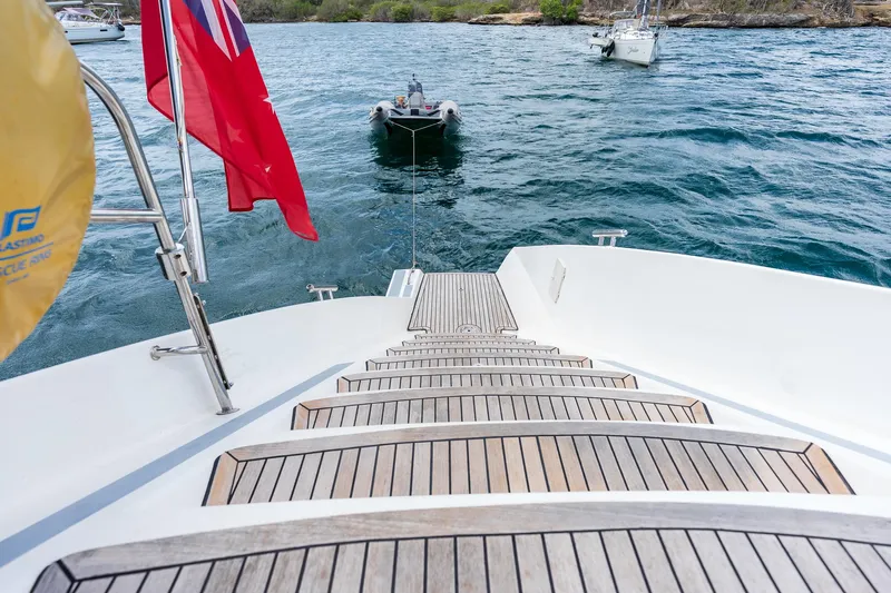 Orion Yacht Photos Pics Catana 90 yacht stern view with wooden steps, towing a small boat on the water.