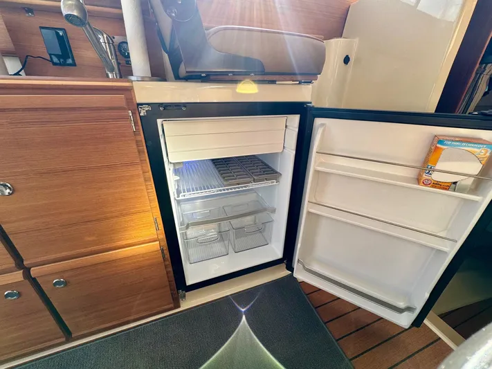  Yacht Photos Pics 2024 Ranger Tugs R-27 interior with open refrigerator, wooden cabinetry, and sunlight streaming in.
