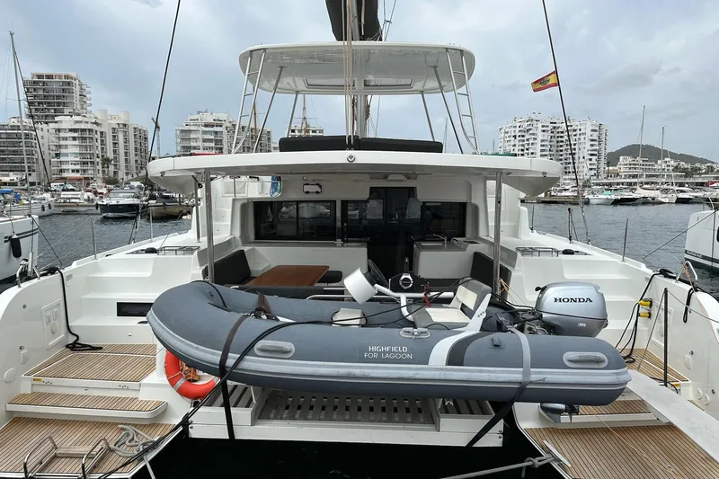 Alegr&iacute;a Yacht Photos Pics 2020 Lagoon 46 catamaran with dinghy, docked in a marina, surrounded by modern buildings.