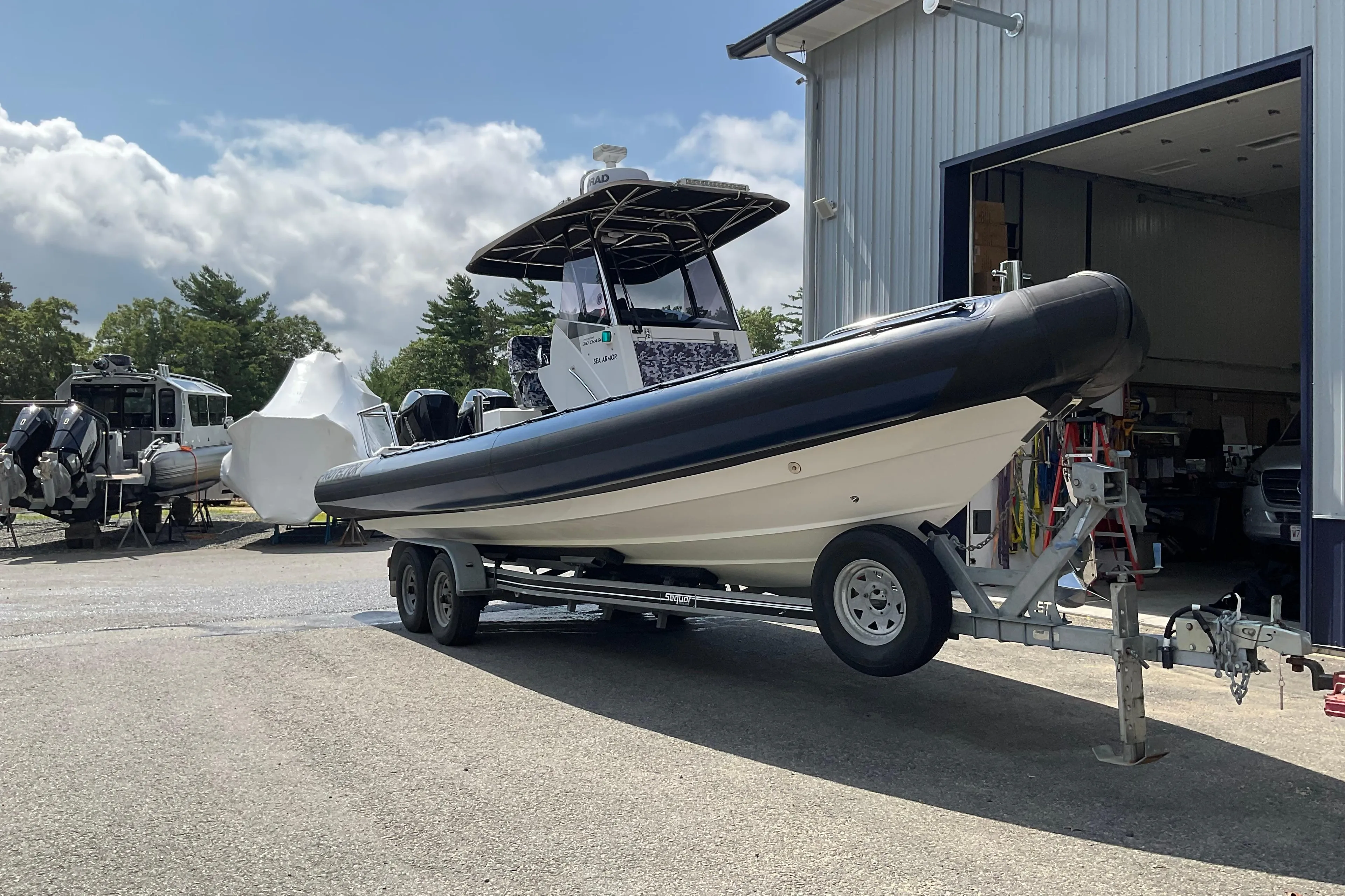 2019 Protector 310 Chase boat on trailer outside a garage, under a partly cloudy sky.