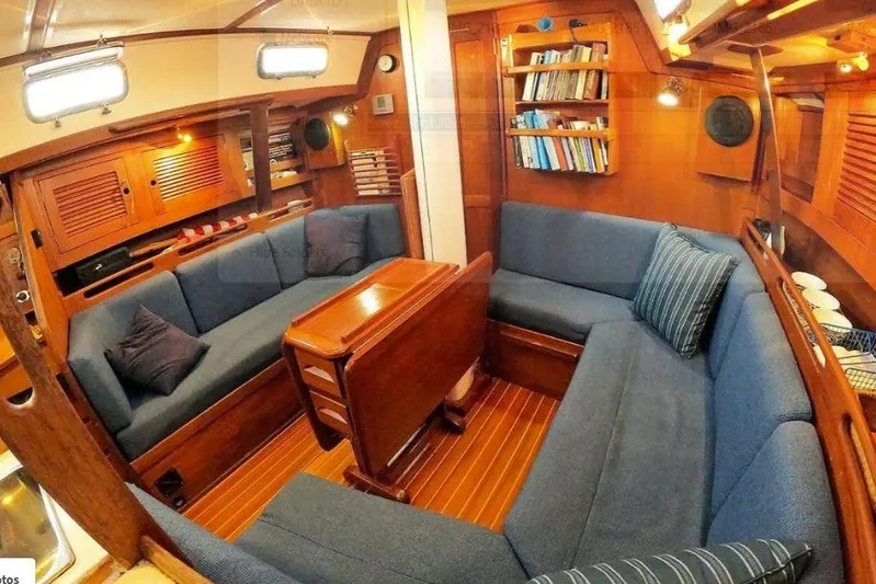 Acadia Yacht Photos Pics Cozy 1997 Tartan 3800 yacht interior with blue seating, wooden table, and bookshelves.