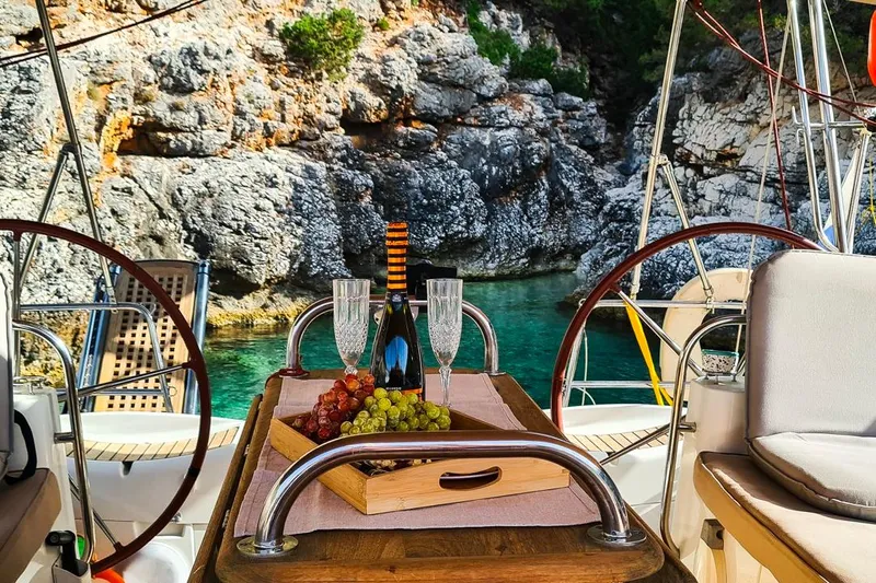  Yacht Photos Pics Luxurious Jeanneau Sun Odyssey 50 DS yacht with wine and grapes, scenic rocky cove backdrop.