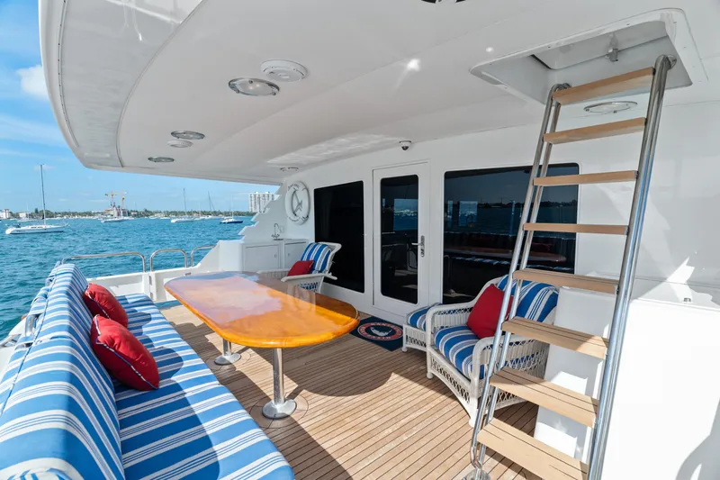 Crown Jewel Yacht Photos Pics Luxury yacht deck with striped seating, wooden table, and ocean view. Broward 96 Raised Pilothouse MY, 1996.