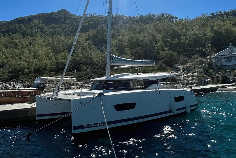  Yacht Photos Pics 2018 Fountaine Pajot Lucia 40 catamaran docked by a scenic, wooded shoreline.