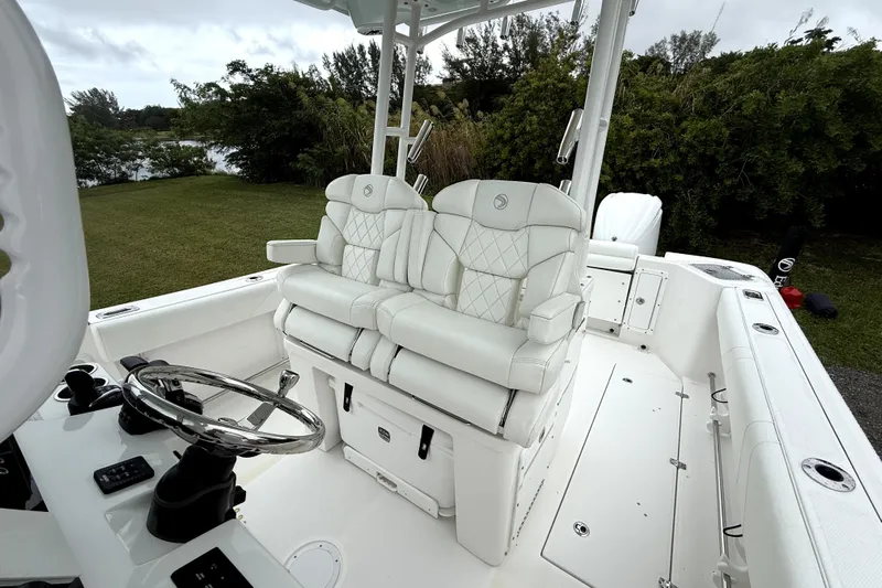  Yacht Photos Pics 2023 Edgewater 285CC boat interior with white seating and steering wheel, surrounded by greenery.