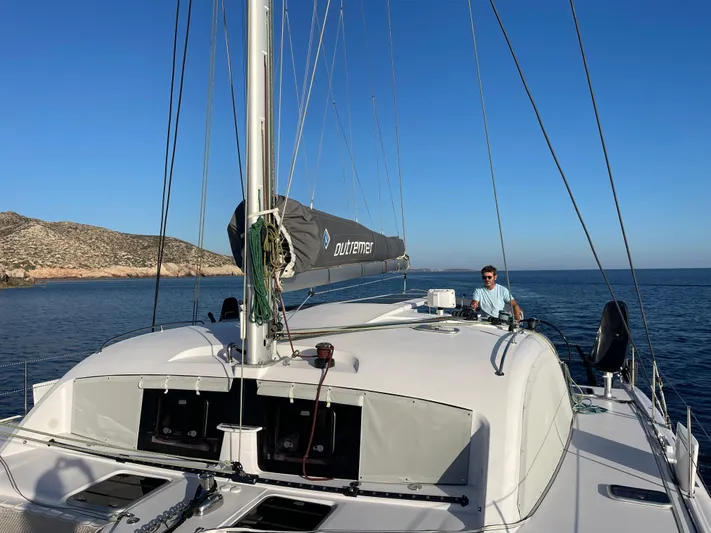 Peems Yacht Photos Pics 2022 Outremer 45 catamaran sailing near rocky coastline under clear blue sky.