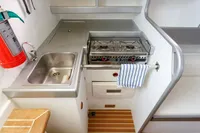 Compact galley kitchen in 2012 Puffin 30 Sloop, featuring stove, sink, and fire extinguisher.