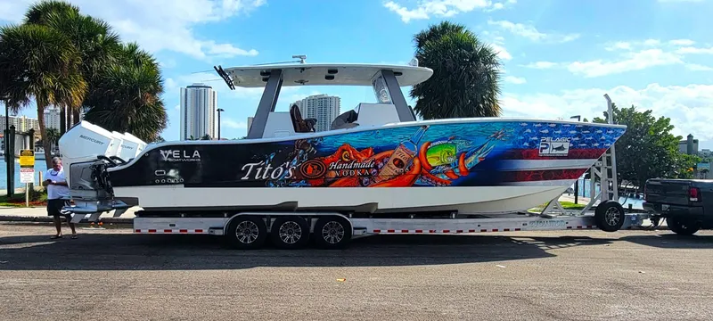  Yacht Photos Pics 2021 Vela 368 Center Console boat with vibrant graphics on a trailer, parked near palm trees.