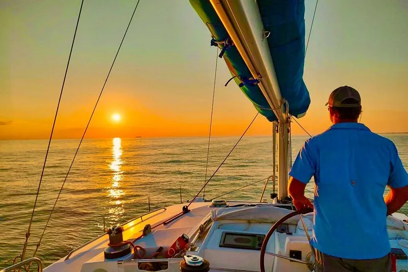 Liberty Yacht Photos Pics Man steering Lagoon 440 catamaran at sunset, 2005 model, serene ocean view.