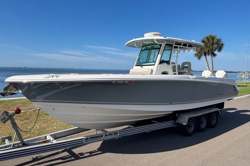  Yacht Photos Pics 2021 Boston Whaler 330 Outrage boat on trailer by waterfront, clear sky background.