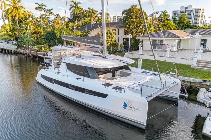  Yacht Photos Pics 2022 Leopard 45 catamaran docked by a waterfront property with lush palm trees.