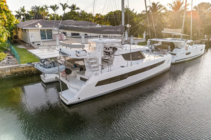  Yacht Photos Pics 2022 Leopard 45 catamaran docked by a waterfront home, surrounded by lush greenery.