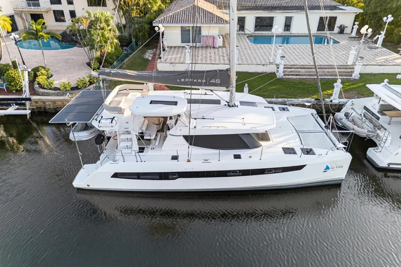  Yacht Photos Pics 2022 Leopard 45 catamaran docked by a luxurious waterfront property with a pool.