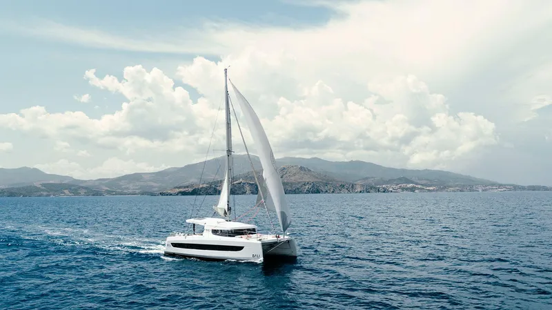 Tbd Yacht Photos Pics Sailing catamaran Bali CATSMART 2026 on open sea with scenic mountain backdrop.