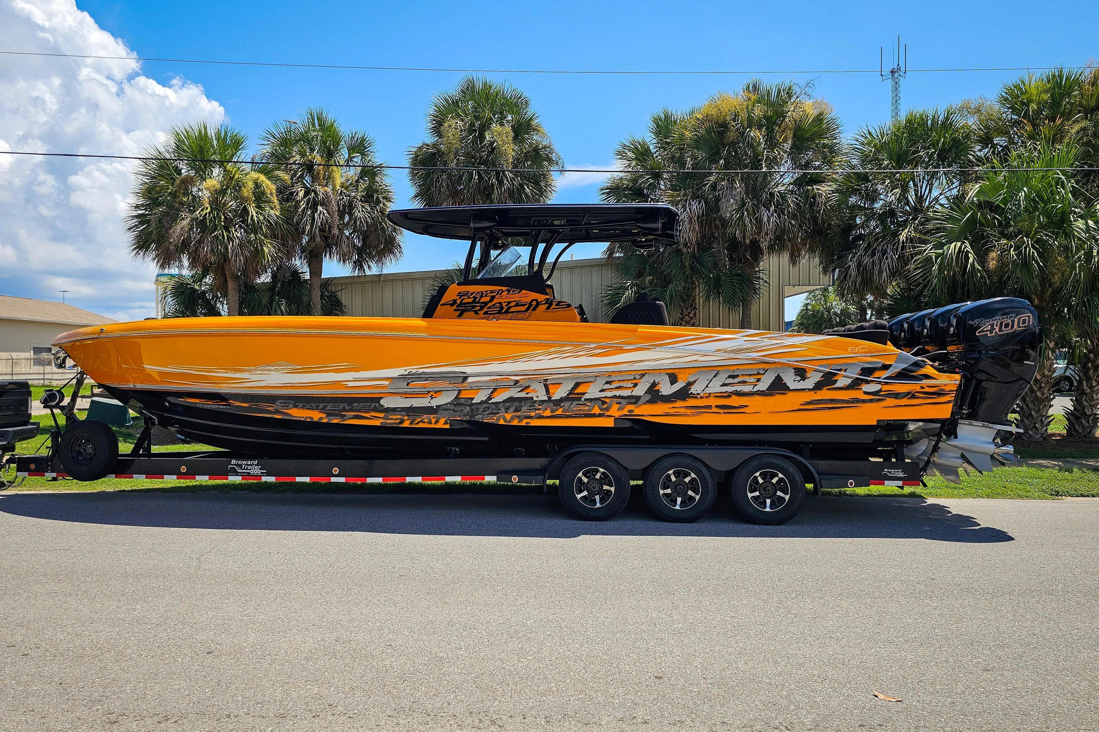 2016 Statement 380 Open boat on trailer, vibrant orange design, parked near palm trees.